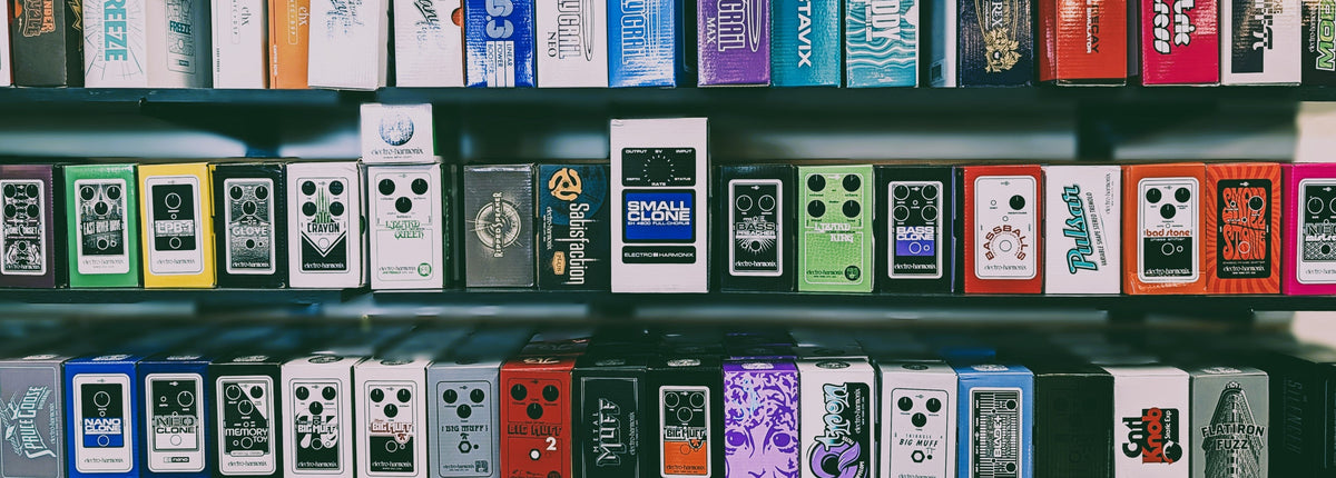 Rows of guitar effect pedals and amplifiers in colorful retail packaging, arranged neatly on dark shelves.